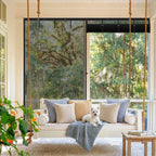 A small white dog lying on a porch swing bed in front of a roll-up magnetic screen enclosure.